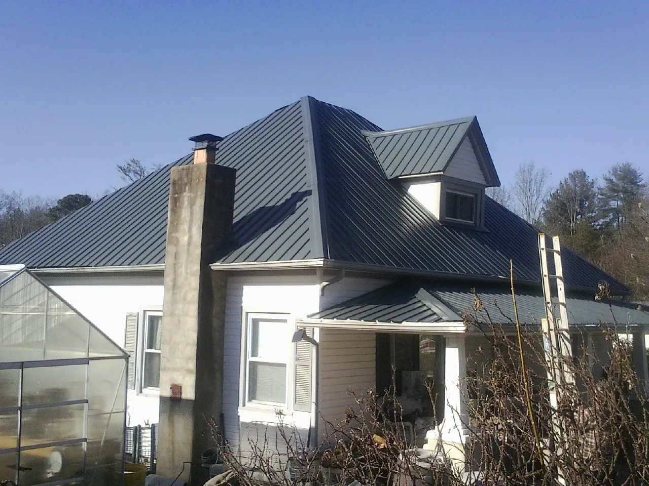 Dark blue standing seam metal roof on a white farmhouse with dormer — Slate & Tile Roof Repair by Roofing Brothers in Ennice