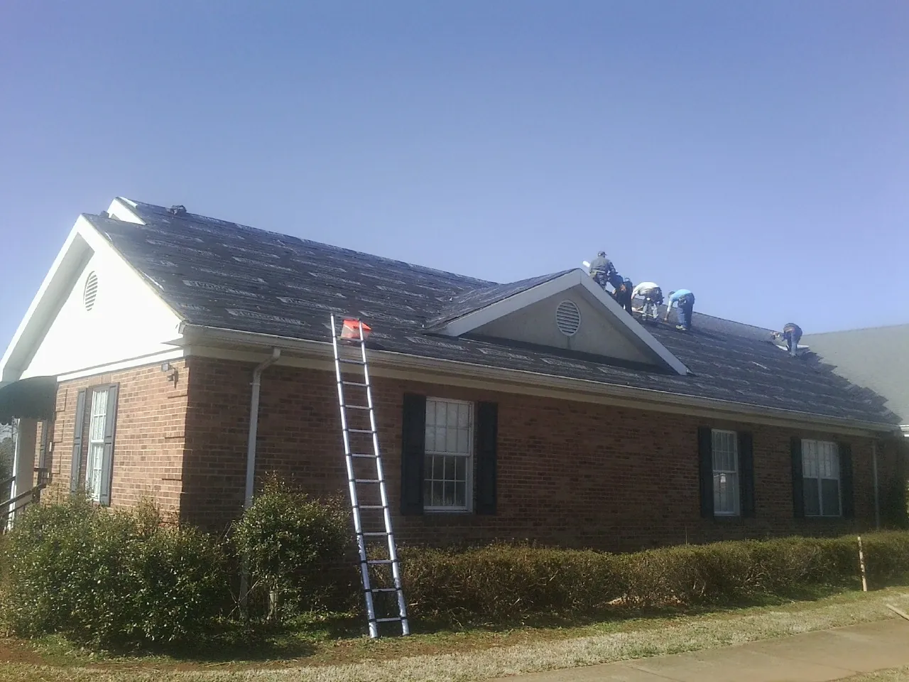 Crew tearing shingles off a brick ranch roof with a ladder set — Metal Roof Repair work by our crew in Ennice