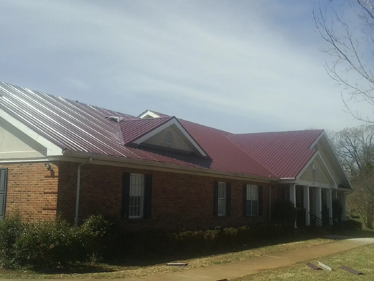 Red metal roof with gabled entries on a long brick building, from a Hail Damage Roof Repair job in Ennice