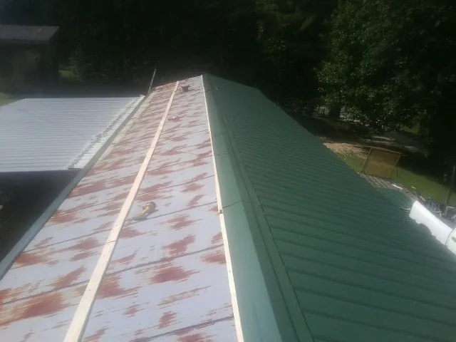 Old rusted panels beside newly installed green metal roofing — Wind Damage Roof Repair by Roofing Brothers in Ennice