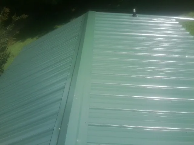 New green metal panels meeting at the ridge of a roof — Flat Roof Repair work by our crew in Ennice