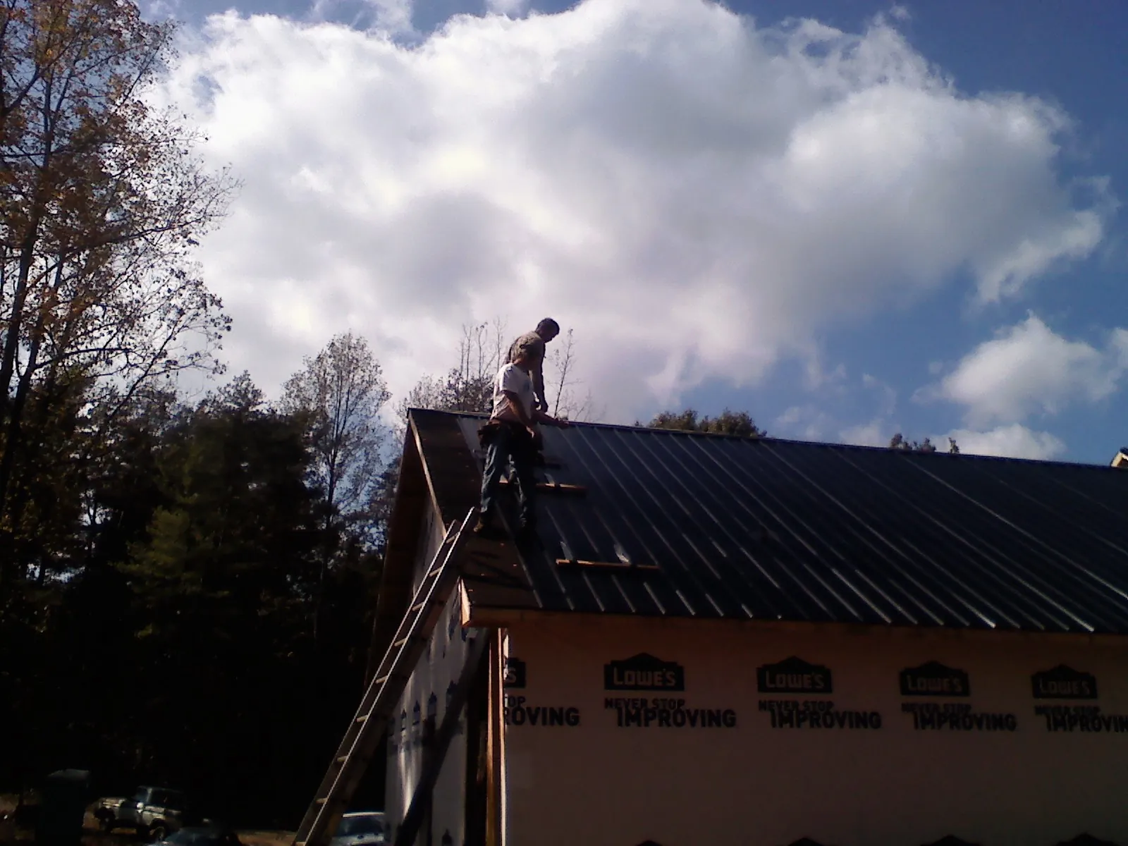 Roofer fastening dark metal panels high against a cloudy sky, from a Roof Inspection job in Ennice