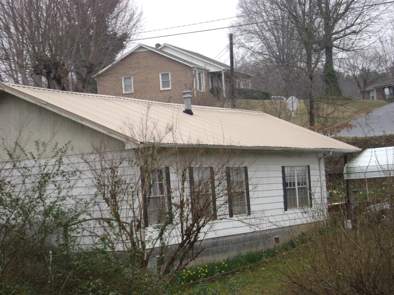 Tan metal roof on a white sided house set into a hillside — Commercial Roofing by Roofing Brothers in Ennice